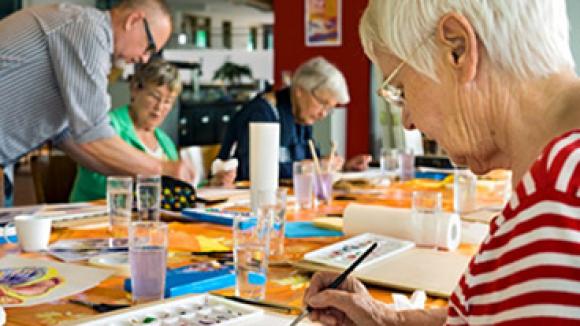 Older woman painting at a table during an art class.
